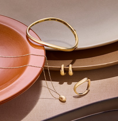 Image of yellow gold bracelet, necklace, earrings and rings on cream background. tap to shop all yellow gold jewellery image