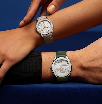 Two wrists wearing beige and green Piaget watches against a dark blue background. image
